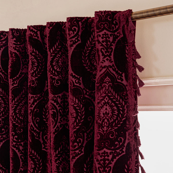 Close-up of a burgundy patterned curtain with tassels on a beige background