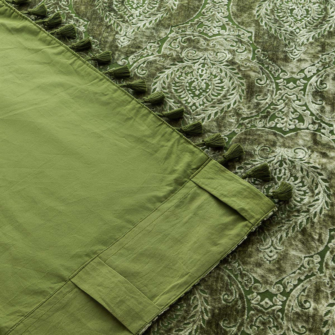 Moss green velvet curtain with a damask pattern and tasseled edge. The corner of the curtain is flipped up to show the cotton backing.