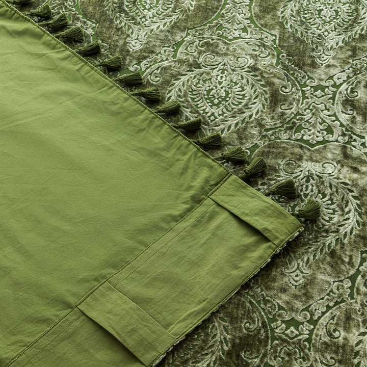 Moss green velvet curtain with a damask pattern and tasseled edge. The corner of the curtain is flipped up to show the cotton backing.