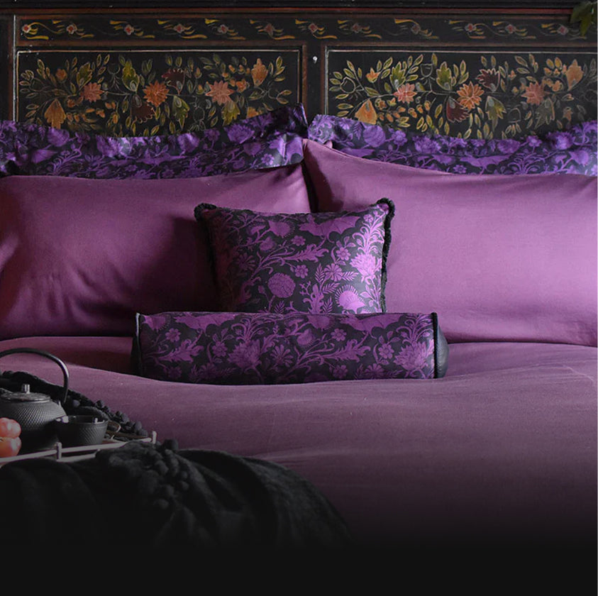 Purple bamboo bedding set with botanical pillows on a bed with an ornate headboard.