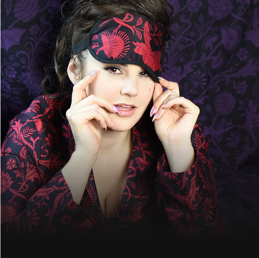 Woman wearing a red and black Elysian Fields patterned eye mask against a purple Elysian Fields background
