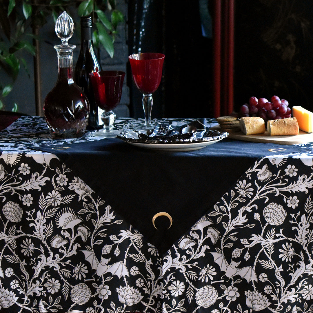 A black and white gothic botanical tablecloth setting with food. Tablecloth is in Sin in Linen's Elysian Fields print